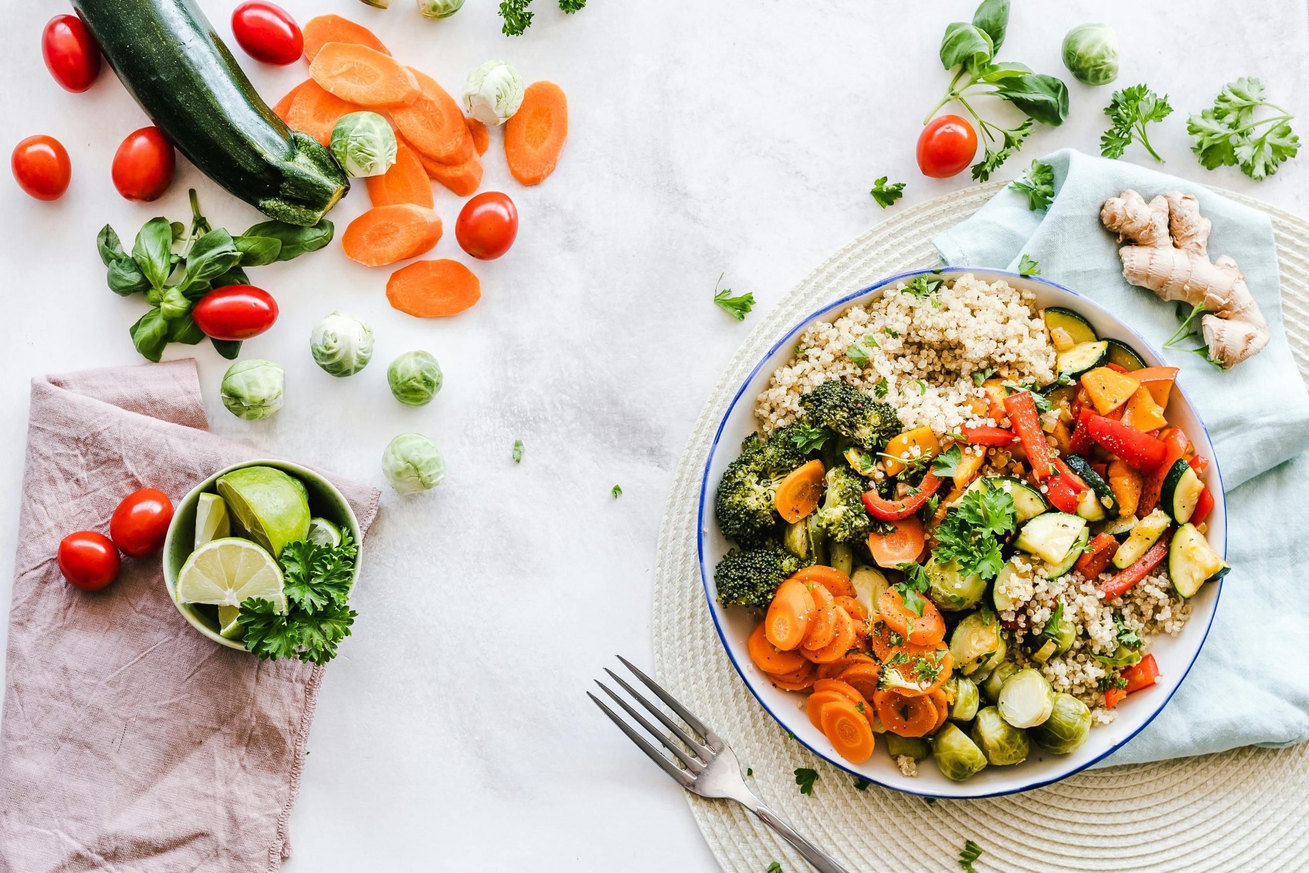 A salad in a bowl, with fresh fruit and vegetables and a fork scattered beside it.