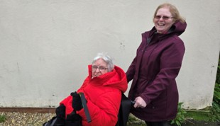 A person being supported by a carer in a wheelchair outside
