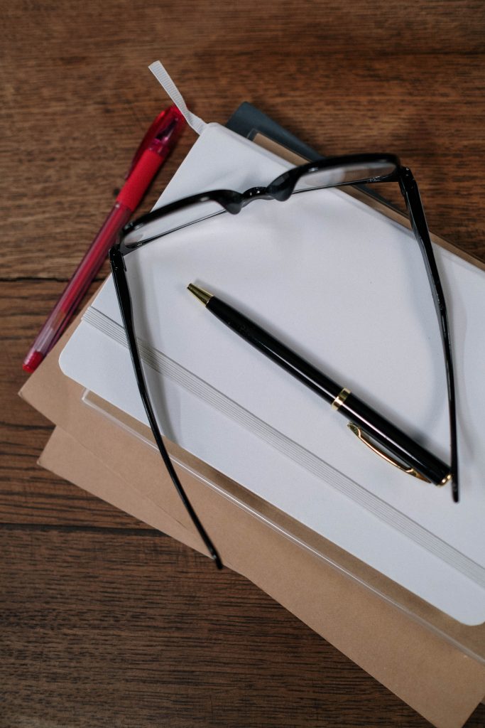 A notepad, pens, and a pair of glasses on a table